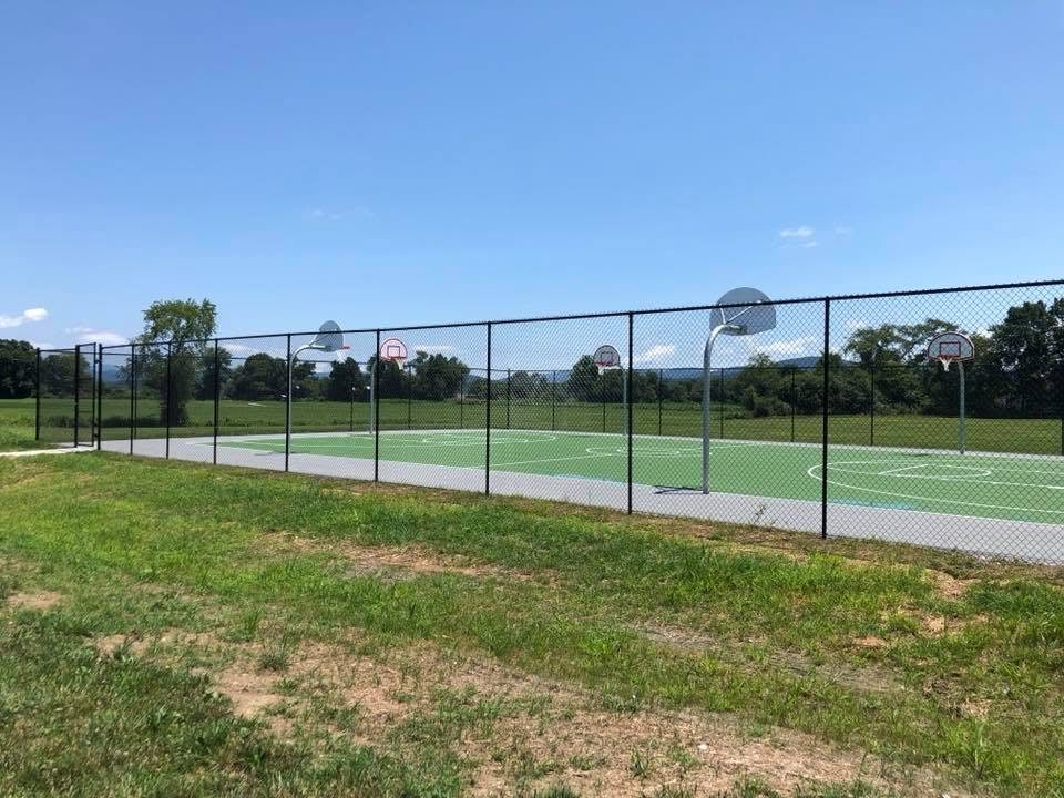 Long run of tall black chain-link fence around outdoor ball courts with the mountains behind