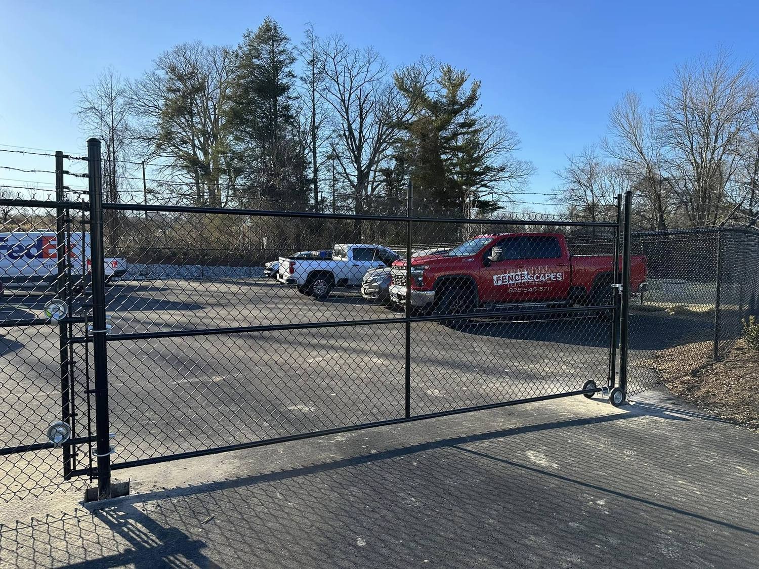 Black vinyl-coated chain-link fence with a rolling gate at a commercial lot