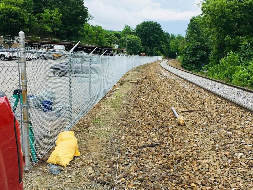 Galvanized chain-link fence with barbed arms running alongside a rail siding and equipment yard