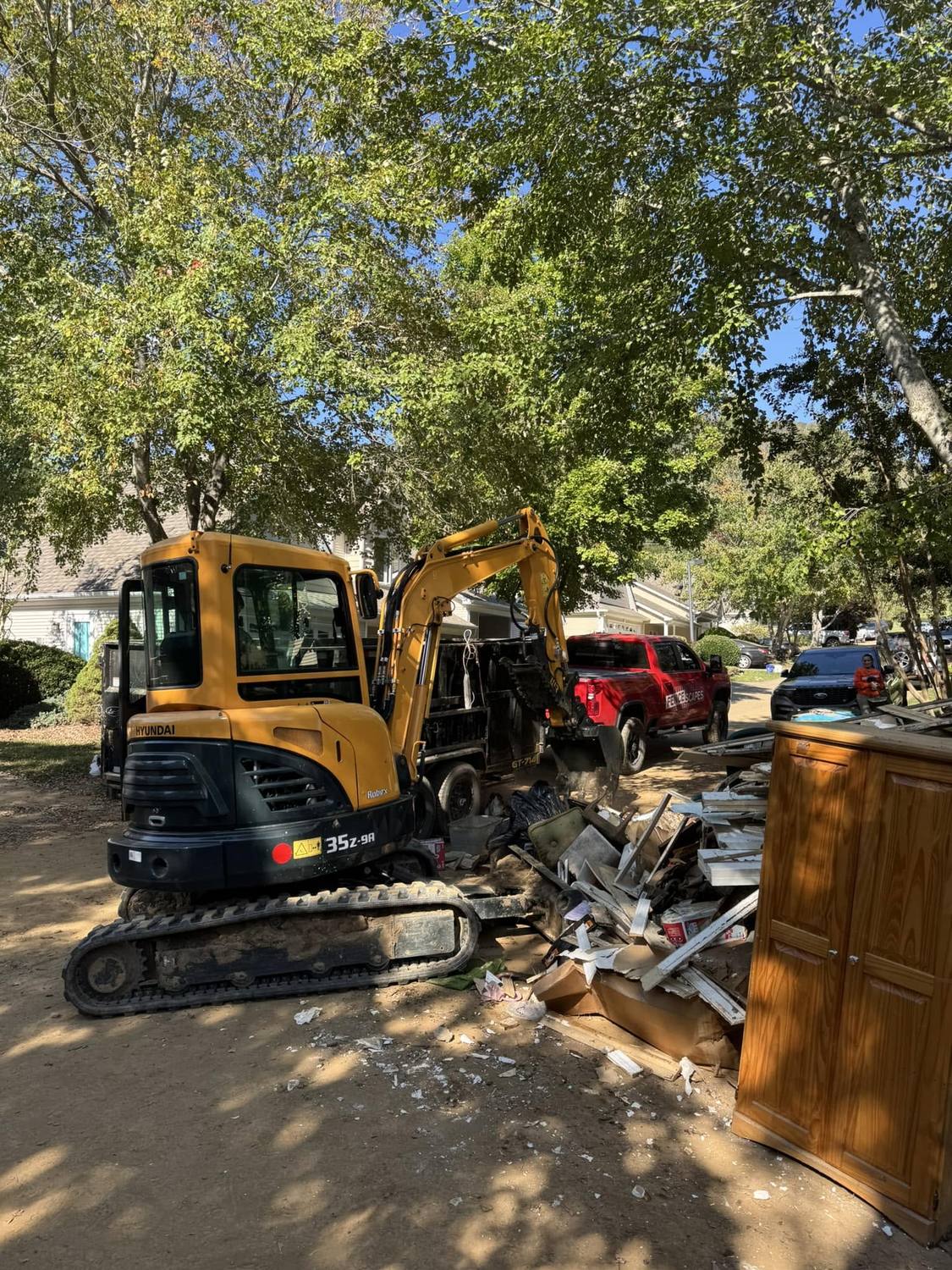 A mini excavator and a Fence Scapes pickup beside a pile of old fence material being cleared off a job site