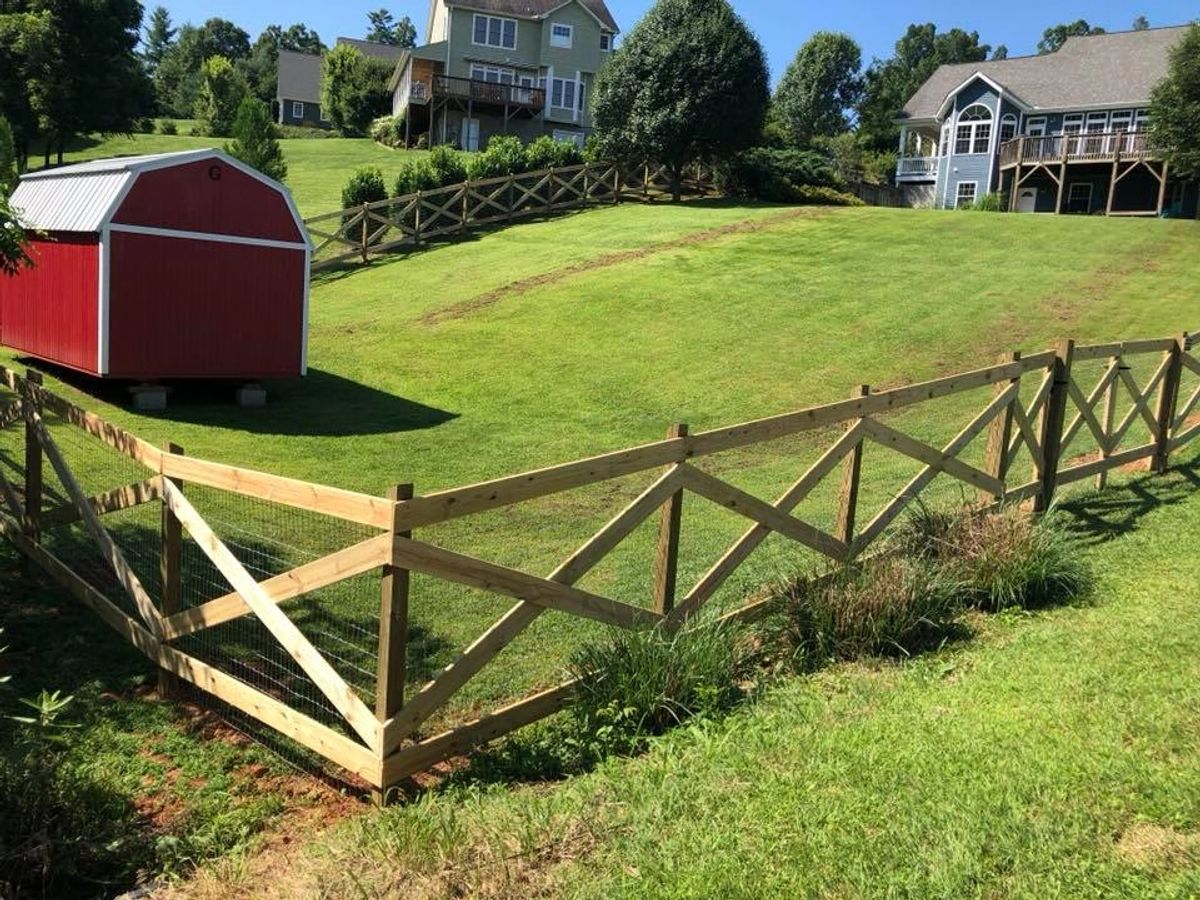 Cross-buck ranch rail fence with wire mesh beside a red barn