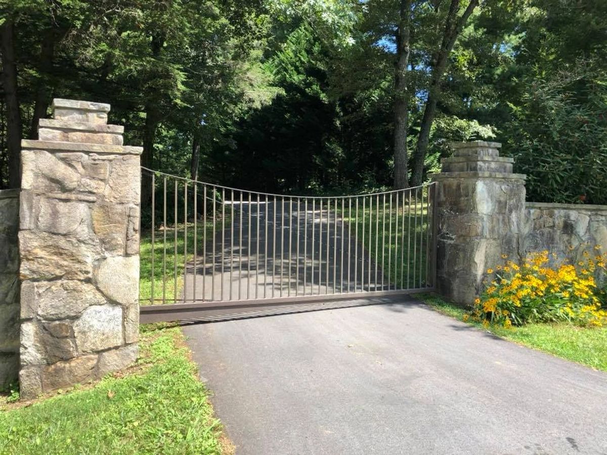 Black iron swing gate between stone pillars