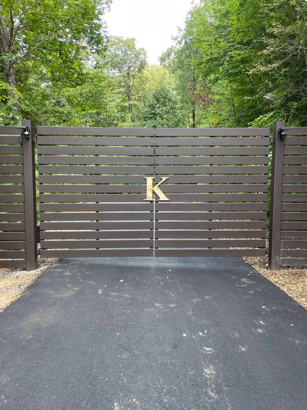 Bronze horizontal-slat driveway gate with gold monogram