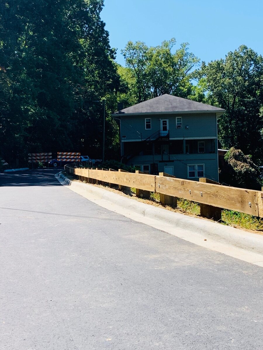Timber post-and-rail guardrail edging a paved driveway entrance below a three-story house