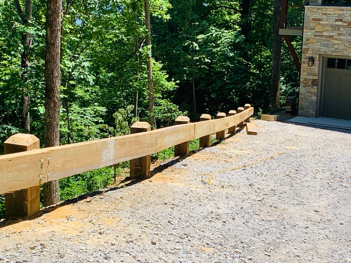 Timber post-and-rail guardrail running along a gravel drive up to a stone-faced garage