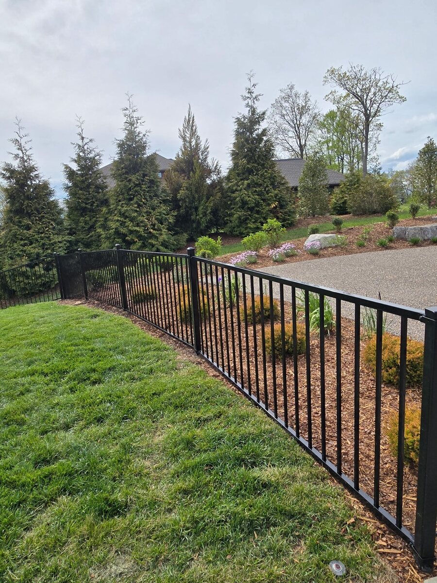 Black aluminum picket fence running along the edge of a landscaped slope with new plantings