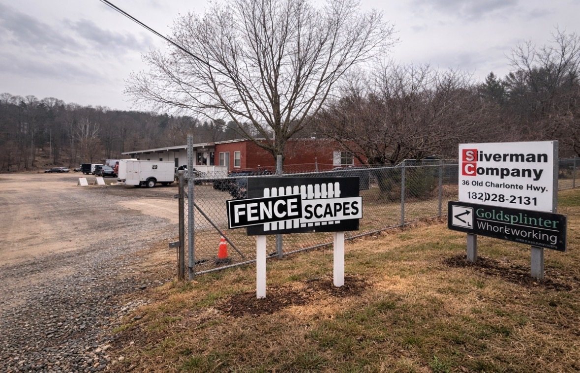 The Fence Scapes shop sign at 36 Old Charlotte Highway in Asheville, with chain-link fence behind it
