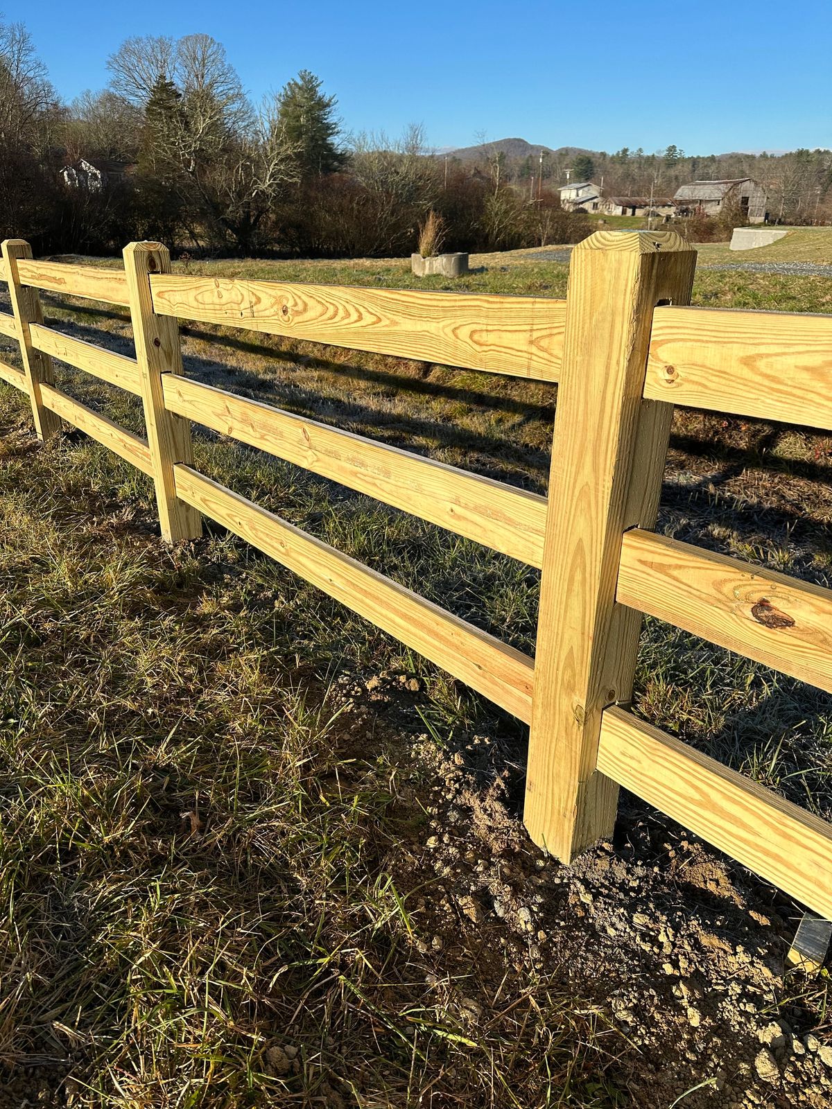 Three-rail wood ranch fence along a pasture with mountain views