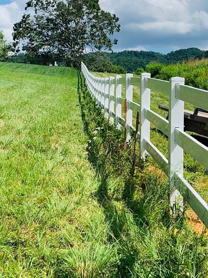 White vinyl three-rail fence with wire mesh backing along a green pasture