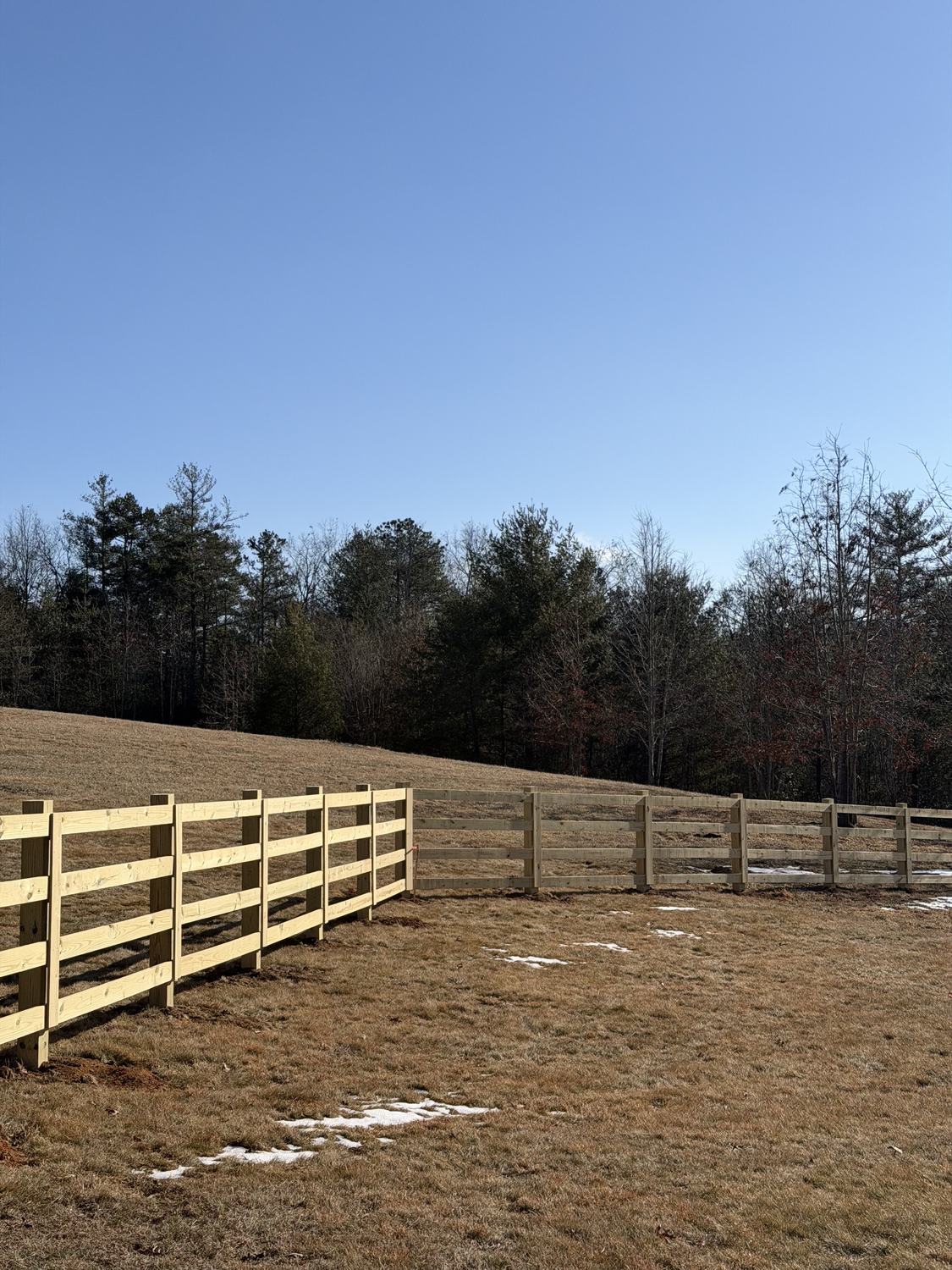 Four-rail wood fence stepping down a slope