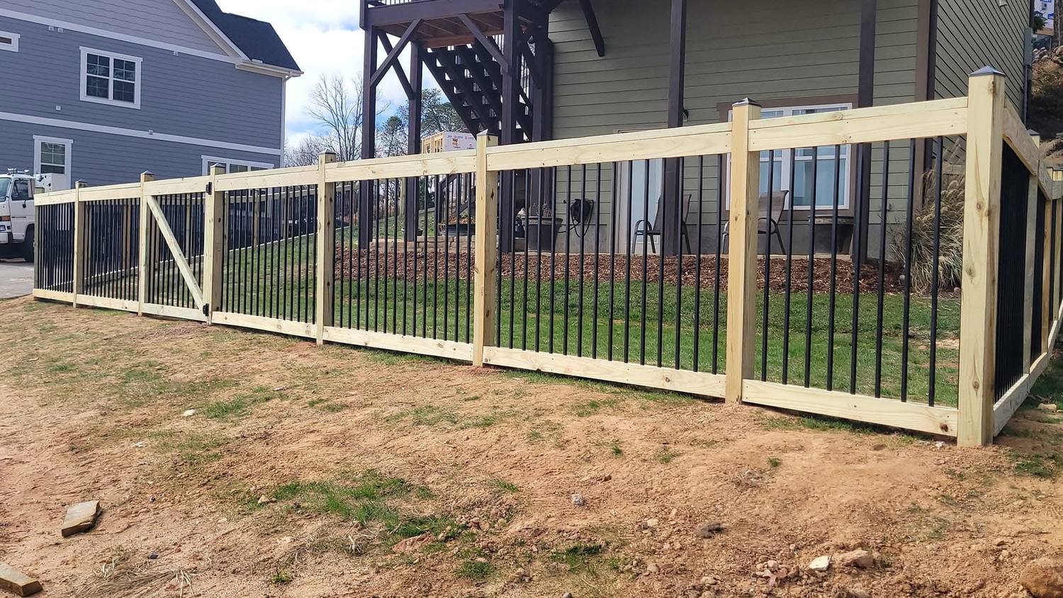 Wood posts and rails framing black aluminum fence panels along the back of a newly built house