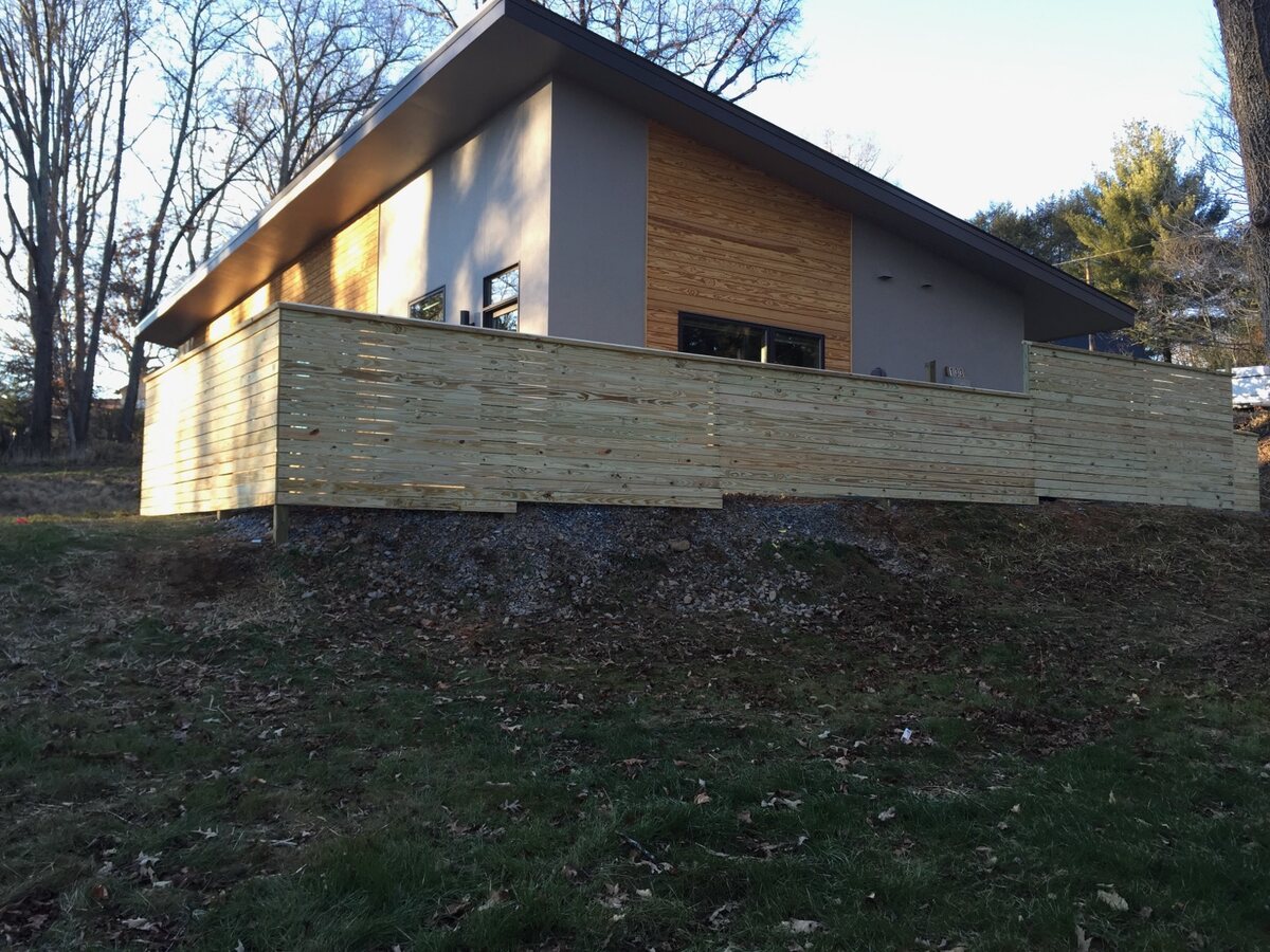 Horizontal-board wood fence running along a graded slope in front of a modern home