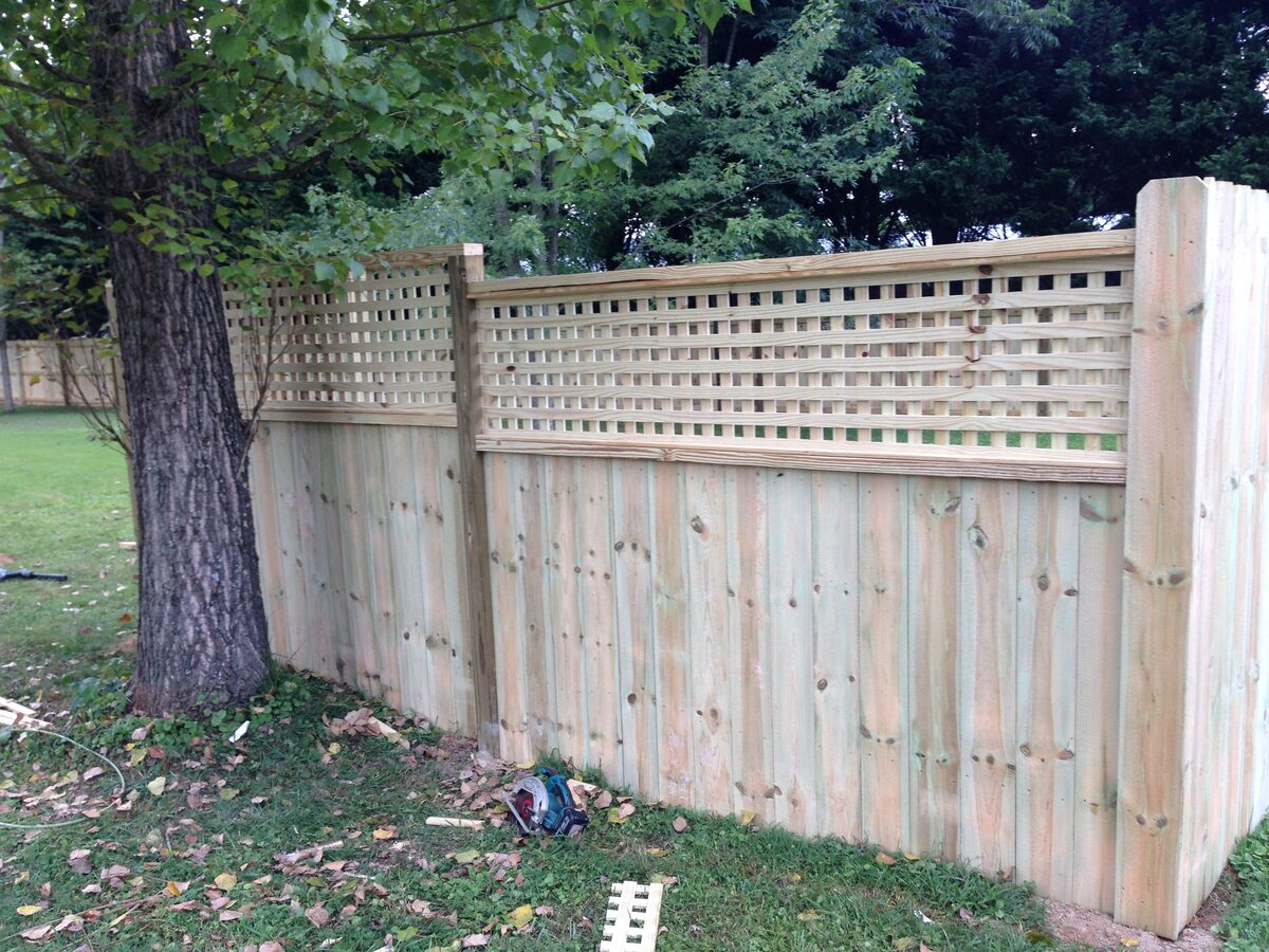 Tall wood privacy fence with a square lattice topper running along a wooded back yard