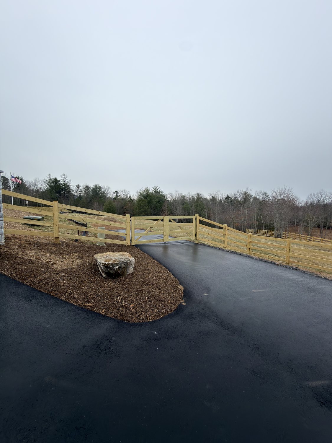 Wood three-rail fence and matching gate along a paved driveway entrance